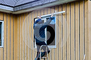 Exterior finishing work on frame and panel house on facade side, roofer installs window opening jambs.