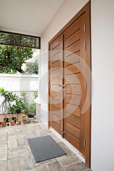 Exterior of a house with wooden door, gray tiled floor and plant.