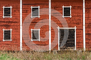 Exterior of old abandoned decayed red barn with closed wooden window shutters.