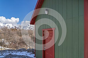 Exterior of a storage shed with a lamp on the green wall above the red door