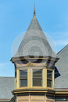 Exterior turret or spire with beige stucco home or house and gray slatted roof with spike on pinacle
