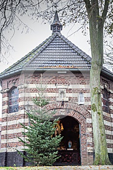 Exterior view of the Chapel of Mary in de Nood on a small hill with its gray dome, a Christmas tree next to the door