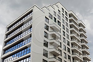 Exterior view of contemporary tall apartment building premises with wide glass windows and balcony