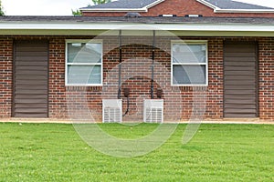 Exterior view of a generic apartment building with older model HVAC heat pumps, twin windows, green grassy lawn, creative copy spa