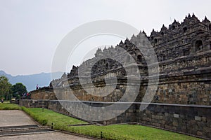 Exterior wall of ancient Borobudur temple view from the base of temple with mountain in background and clear blue sky