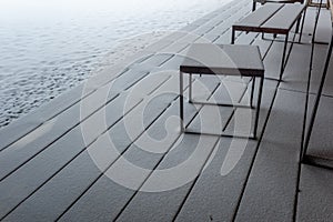 Exterior wooden terrace with wooden outdoor furniture covered with snow.