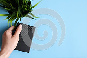The external hard drive is black in the female hand and a green plant on a blue background. space for text.