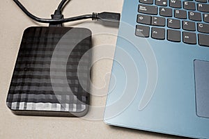 External hard drive with usb cable connected to a laptop or notebook computer on a rustic surface