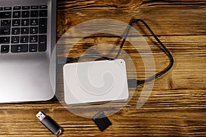 External HDD connected to laptop computer, SD memory card and USB flash drive on wooden desk. Top view. Concept of data storage