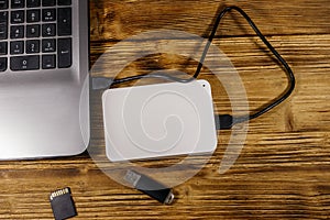 External HDD connected to laptop computer, SD memory card and USB flash drive on a wooden desk. Top view