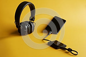 An external portable SSD connected to a smartphone on a yellow background next to wireless headphones. Portable Solid State Drive