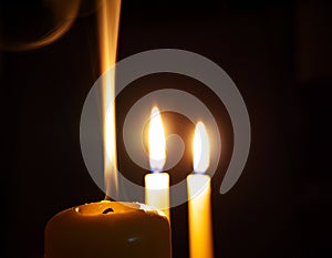 Extinguished candle in front of two burning ones in darkness