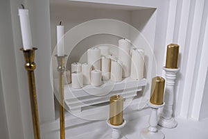 Extinguished round wax white candles of different sizes on a white shelf in the wall