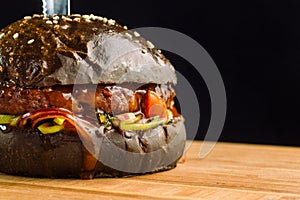 Close-up of delicious fresh home made beef burger with lettuce, cheese, onion and tomato. Black bun.