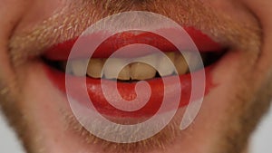 Extra close up of man`s lips with red lipstick. Man with bearded face and red lipstick on lips. Travesty makeup concept