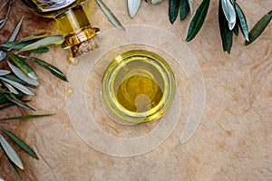 Extra virgin olive oil in glass bowl. It includes olive leaves and branches. Rustic Background. Top view