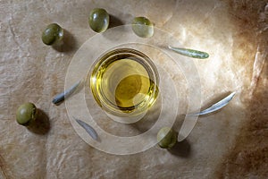 Extra virgin olive oil in glass bowl. It includes olive leaves and branches. Rustic Background. Top view