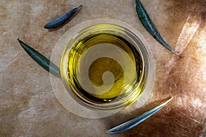 Extra virgin olive oil in glass bowl. It includes olive leaves. Rustic Background. Top view