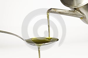 Extra virgin olive oil pouring over a spoon on white background