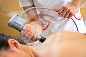 Extracorporeal shockwave therapy in beauty salon. Young woman wearing protective mask during treatment in salon.