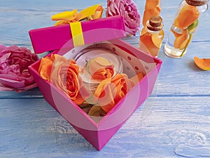 Extract, essence gift box cosmetic product bow composition cream beautiful fresh orange rose on a blue wooden background