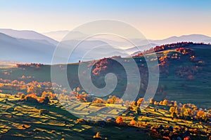 Extraordinary autumn landscape. Green fields with haystacks. Trees covered with orange and crimson leaves. Mountain landscapes.