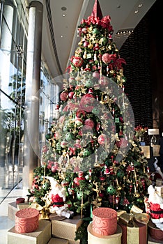Extraordinary Christmas tree, richly decorated with hangings like green balls, red ribbons, toys .Gifts arround the tree.