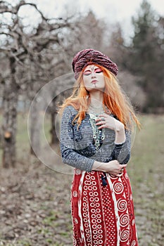 Extravagant redhead woman in ethnic national dress dancing or posing in a mystical forest