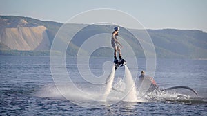 Extreme athlete is using flyboard on sea, moving legs and torso to control movements in summer day