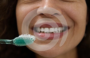 Extreme close-up of the beautiful smile of a woman with clean white teeth, holding a toothbrush near her mouth