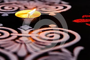 Extreme close up of glowing tea lamp and white red rangoli art on black background. diwali concept