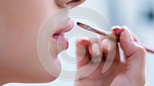 Extreme close up hand make-up artist making makeup of lips using brush