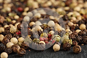 Extreme close up of a mix of black, red, green and white peppercorns on a black, rustic stone kitchen board. Shallow depth of fiel