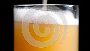 Extreme close-up pouring stream of craft golden beer into transparent glass slowmo