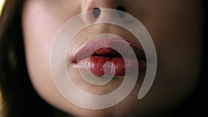 Extreme close up of sexy glossy lips. Young woman pursing her lips in a sexy seductive gesture. Slow motion. Front view