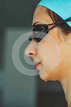 Extreme close-up shot of a Caucasian girl head with a swimming cap and hands putting swimming goggles, preparing for