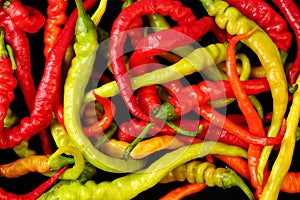 Extreme close up, top down view of many fresh, organic cayenne chili peppers in different colors on a black background