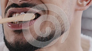 Extreme close-up unrecognizable bearded man brushing teeth with white paste whitening agent with wooden toothbrush clean