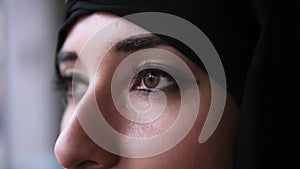 Extreme close-up of a young middle eastern muslim woman in black hijab opening dark brown eyes and looking forward