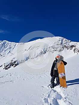 Extreme female snowboarder poses with her board before riding snowy mountain.