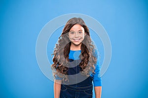 Extreme hair volume. Kid girl long healthy shiny hair. Kid happy cute face with adorable curly hairstyle stand over blue