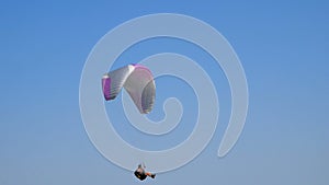 Extreme paraglider flying against a clear blue sky, sunbeam shines into camera. Paraglide flight experience skydive