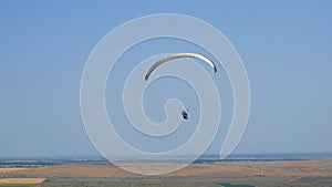 Extreme paraglider flying against a clear blue sky, sunbeam shines into camera. Paraglide flight experience skydive