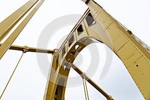 Extreme upward view of a self anchored suspension bridge painted bright yellow against an overcast sky photo