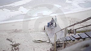 Extreme wide shot of Caucasian woman holding wheelchair with crippled boy. Top view of disabled young man and his mother