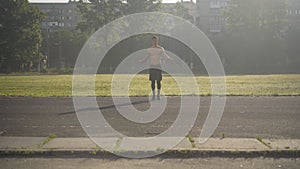 Extreme wide shot of sportive Caucasian sportsman jumping rope in sunlight. Portrait of athletic young man training in