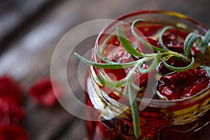 Extremely close-up the jar of homemade sun-dried tomatoes with Provencal herbs, garlic and olive oil on a rustic wooden surface,