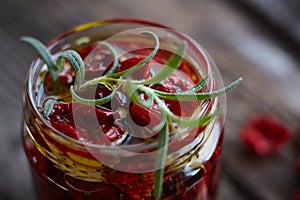 Extremely close-up the jar of homemade sun-dried tomatoes with Provencal herbs, garlic and olive oil on a rustic wooden surface,