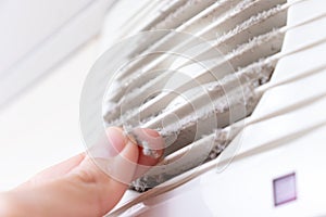 Extremely dirty and dusty white plastic ventilation air grille at home close up and a hand holding dust by fingers, harmful for