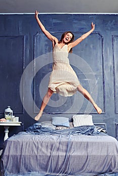 Extremely excited woman in nightgown jumping on bed with arms an